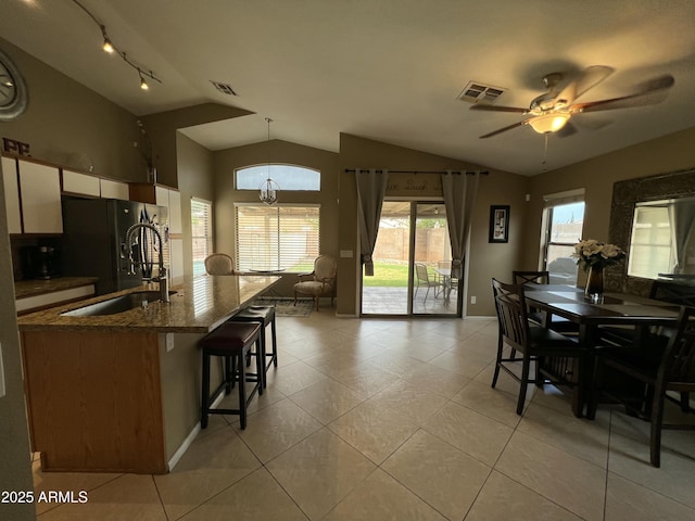 dining area with vaulted ceiling, light tile patterned flooring, ceiling fan with notable chandelier, and visible vents