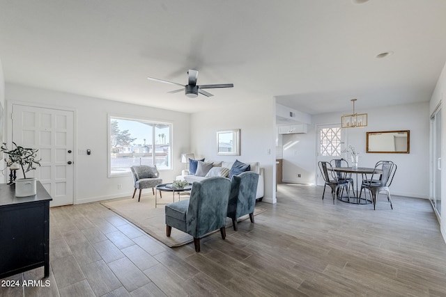 living room with ceiling fan with notable chandelier and light hardwood / wood-style flooring