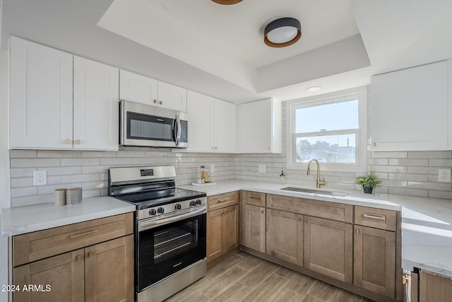 kitchen with appliances with stainless steel finishes, tasteful backsplash, sink, light hardwood / wood-style floors, and white cabinetry