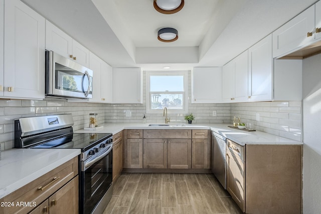 kitchen with white cabinetry, sink, tasteful backsplash, light hardwood / wood-style floors, and appliances with stainless steel finishes