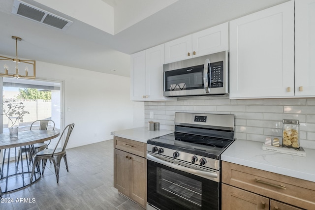 kitchen with hanging light fixtures, stainless steel appliances, light stone counters, backsplash, and white cabinets