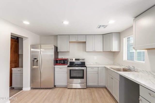 kitchen with sink, light wood-type flooring, appliances with stainless steel finishes, a barn door, and gray cabinets