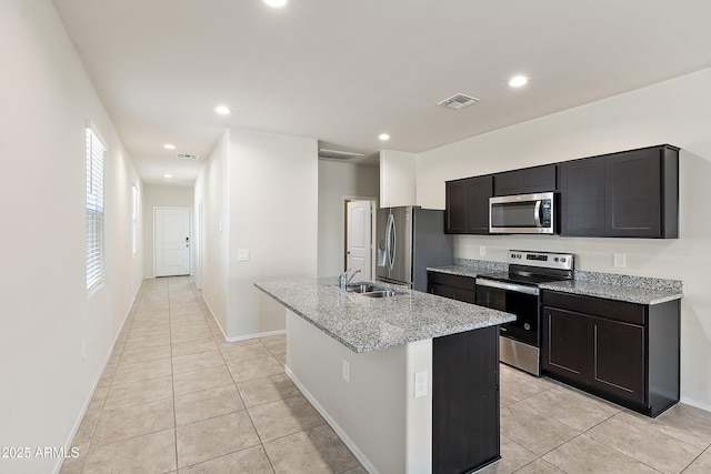 kitchen featuring light tile patterned flooring, appliances with stainless steel finishes, a sink, an island with sink, and visible vents