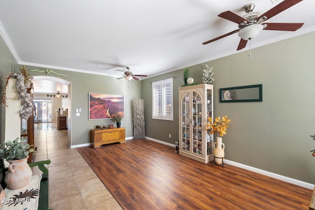 living room with arched walkways, wood finished floors, a ceiling fan, baseboards, and crown molding