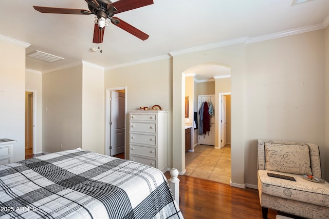 bedroom with arched walkways, crown molding, visible vents, wood finished floors, and baseboards