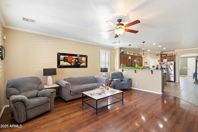 living area with arched walkways, a ceiling fan, visible vents, dark wood-style floors, and crown molding