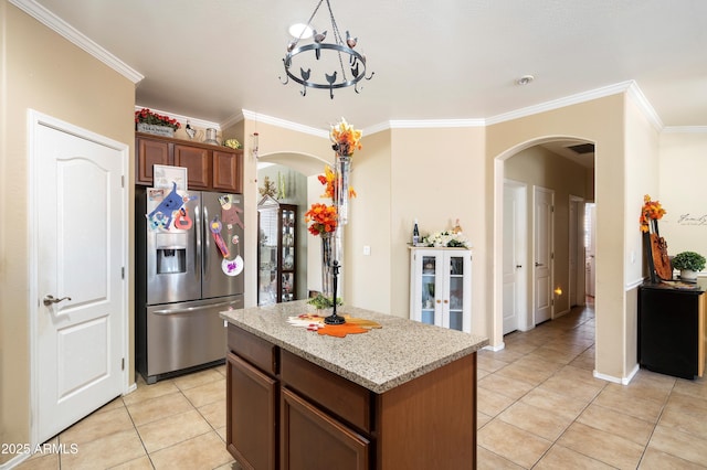 kitchen featuring arched walkways, a center island, stainless steel refrigerator with ice dispenser, ornamental molding, and light stone countertops