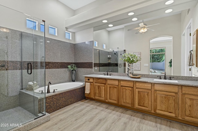 bathroom featuring ceiling fan, vanity, independent shower and bath, hardwood / wood-style flooring, and a towering ceiling