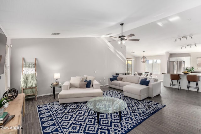 living area with lofted ceiling, visible vents, dark wood-type flooring, baseboards, and ceiling fan with notable chandelier