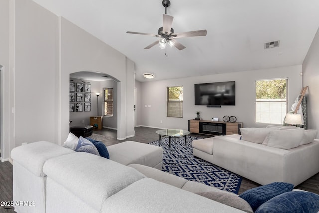 living room featuring lofted ceiling, visible vents, plenty of natural light, and arched walkways