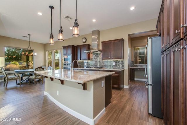 3285 Big Sky Dr, Wickenburg, AZ 85390 - kitchen with wall chimney exhaust hood, appliances with stainless steel finishes, tasteful backsplash, a kitchen breakfast bar, and light stone counters