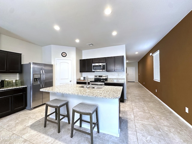 kitchen featuring light stone countertops, stainless steel appliances, recessed lighting, a sink, and an island with sink