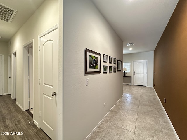 corridor with baseboards, visible vents, and tile patterned floors