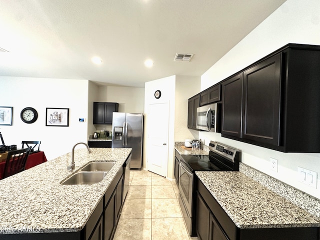 kitchen featuring dark cabinetry, a sink, an island with sink, visible vents, and appliances with stainless steel finishes
