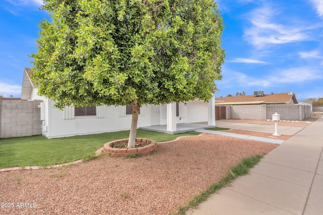 view of property hidden behind natural elements with a garage, driveway, a front yard, and fence