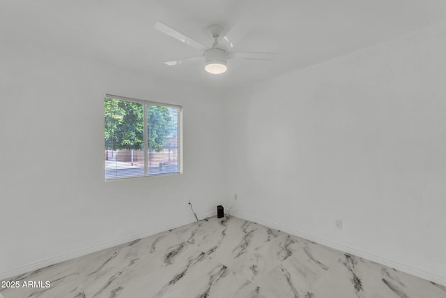 spare room with a ceiling fan, marble finish floor, and baseboards