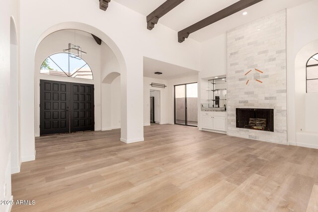 8725 E Via Del Arbor, Scottsdale, AZ 85258 - unfurnished living room with a towering ceiling, light wood-type flooring, plenty of natural light, beamed ceiling, and a tile fireplace