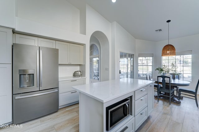 kitchen featuring light stone counters, stainless steel appliances, visible vents, light wood-type flooring, and pendant lighting