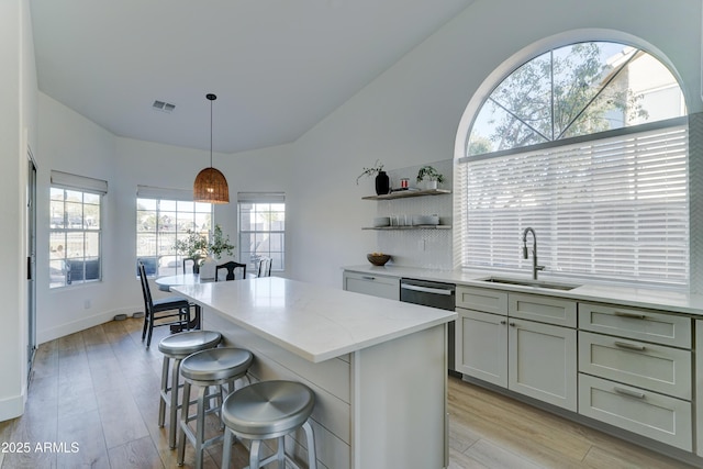 kitchen featuring visible vents, a center island, hanging light fixtures, open shelves, and a sink