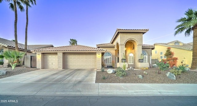 mediterranean / spanish-style house featuring an attached garage, a tiled roof, and stucco siding