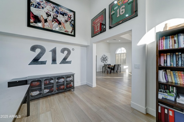 hallway with light wood-style floors, a high ceiling, and baseboards