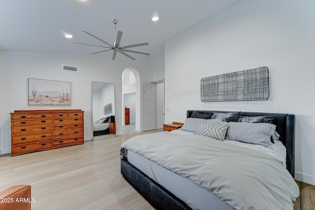 bedroom featuring arched walkways, lofted ceiling, visible vents, baseboards, and light wood-type flooring