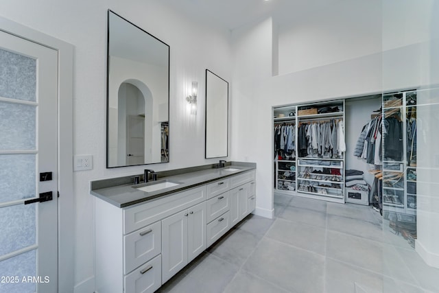 bathroom featuring double vanity, a walk in closet, a sink, and tile patterned floors