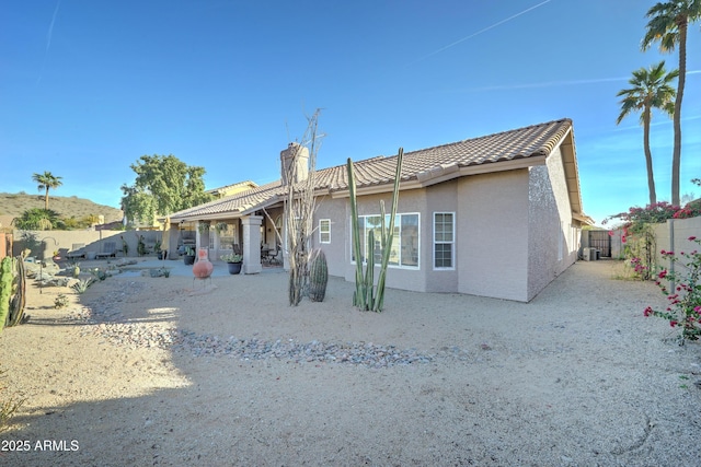 rear view of property featuring a tiled roof, a chimney, a fenced backyard, and stucco siding