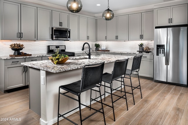 kitchen with light stone counters, sink, an island with sink, light wood-type flooring, and appliances with stainless steel finishes