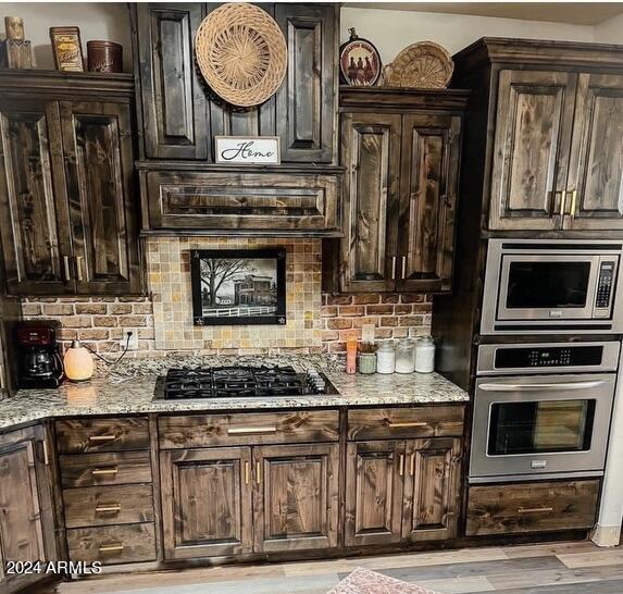 kitchen with light hardwood / wood-style flooring, light stone countertops, dark brown cabinetry, appliances with stainless steel finishes, and tasteful backsplash