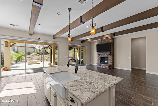 kitchen featuring pendant lighting, beam ceiling, sink, a kitchen island with sink, and white cabinetry