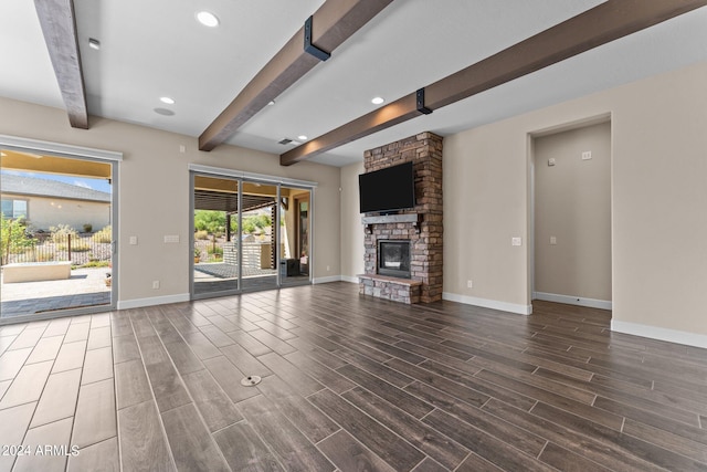 unfurnished living room with dark hardwood / wood-style floors, beam ceiling, and a stone fireplace