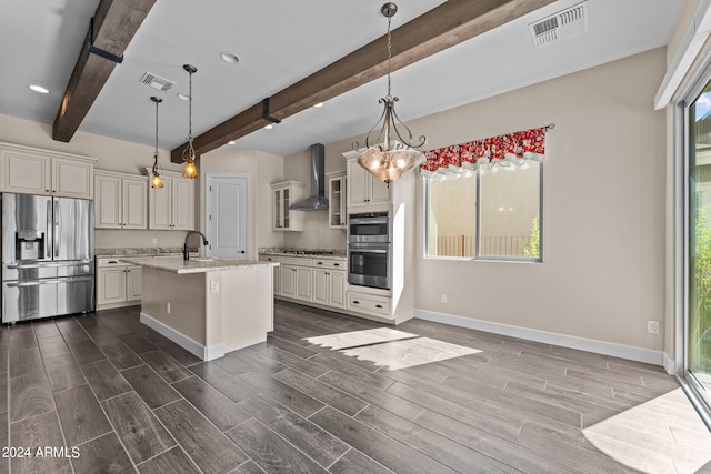 kitchen featuring beam ceiling, wall chimney exhaust hood, a kitchen island with sink, appliances with stainless steel finishes, and dark hardwood / wood-style floors