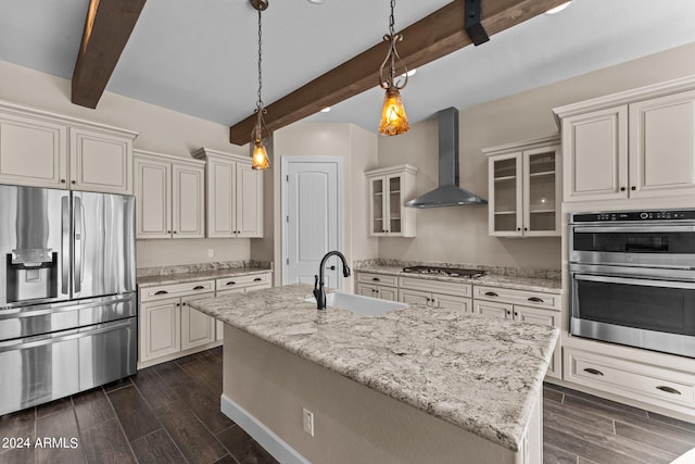 kitchen with an island with sink, sink, beam ceiling, wall chimney exhaust hood, and appliances with stainless steel finishes