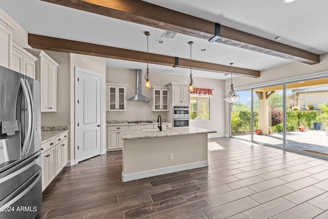 kitchen with wall chimney exhaust hood, pendant lighting, a center island with sink, light stone countertops, and appliances with stainless steel finishes