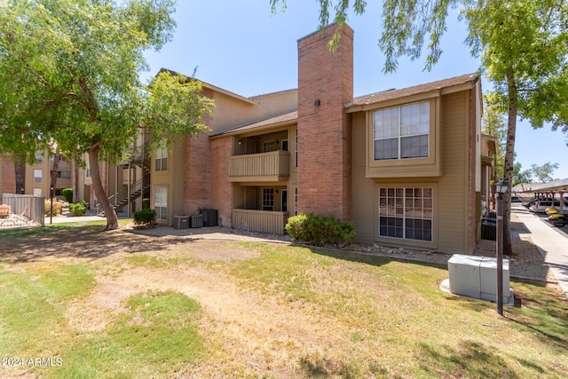 rear view of property featuring a balcony, central AC, and a lawn