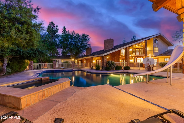 pool at dusk featuring a water slide and a patio