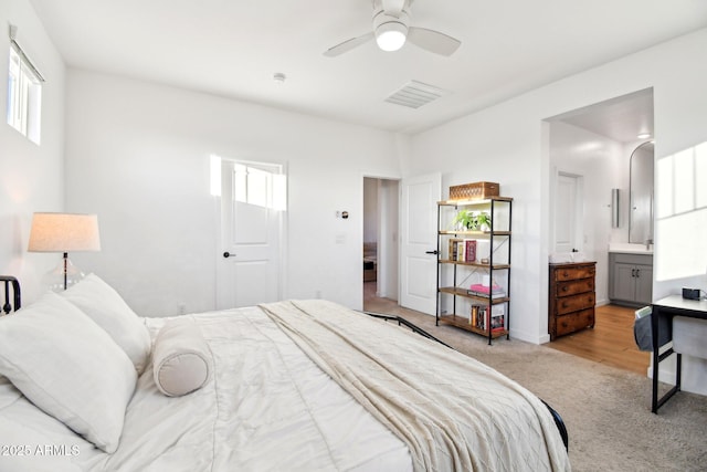 bedroom with connected bathroom, light colored carpet, and ceiling fan