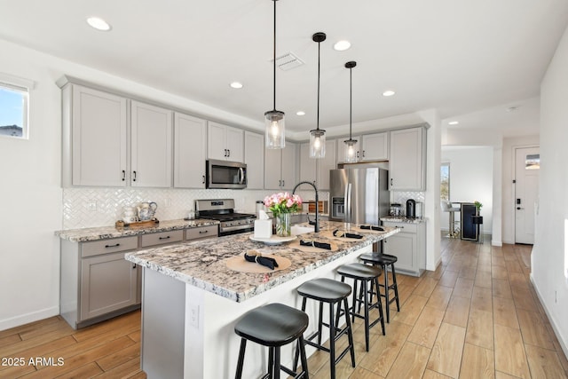 kitchen with appliances with stainless steel finishes, a kitchen island with sink, pendant lighting, and a breakfast bar