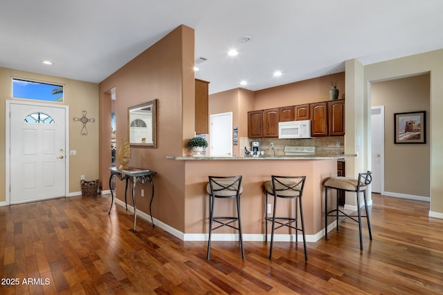 kitchen featuring a breakfast bar area, tasteful backsplash, dark hardwood / wood-style floors, kitchen peninsula, and light stone countertops