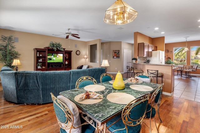 dining space with ceiling fan with notable chandelier and light hardwood / wood-style floors