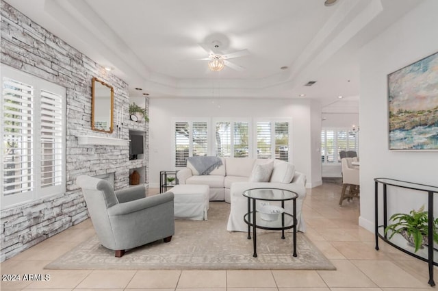 tiled living room with a wealth of natural light, a tray ceiling, and ceiling fan with notable chandelier