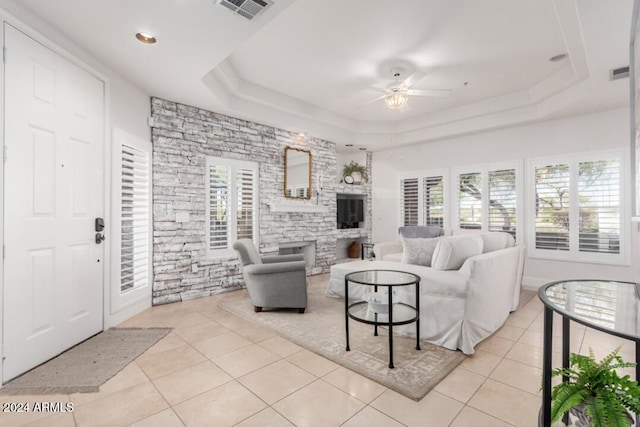 tiled living room with ceiling fan and a raised ceiling