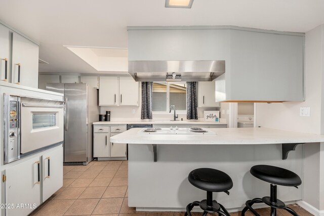 8431 E Rose Ln, Scottsdale, AZ 85250 - kitchen with freestanding refrigerator, light tile patterned floors, a peninsula, a breakfast bar, and light countertops