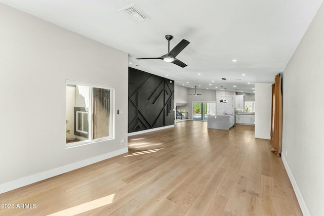 unfurnished living room featuring ceiling fan, a barn door, and light hardwood / wood-style flooring