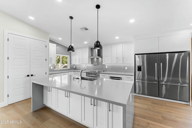 kitchen featuring pendant lighting, sink, appliances with stainless steel finishes, white cabinetry, and an island with sink