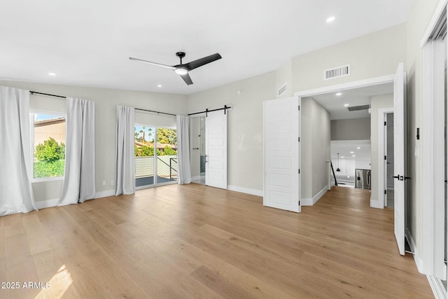 interior space with a barn door, ceiling fan, and light wood-type flooring