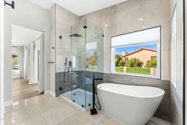 bathroom with tile patterned floors, a healthy amount of sunlight, plus walk in shower, and tile walls