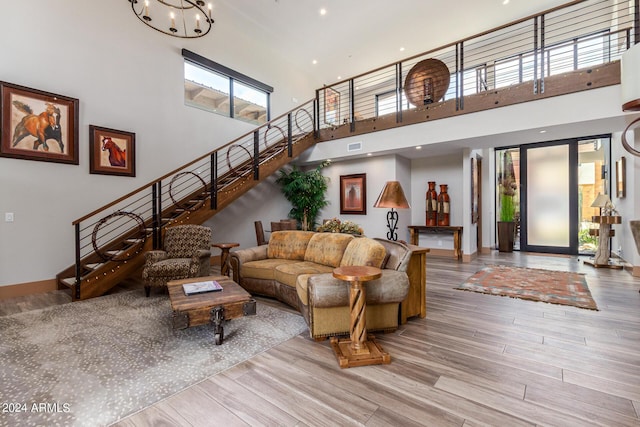 living room featuring a notable chandelier, a healthy amount of sunlight, a towering ceiling, and light hardwood / wood-style flooring