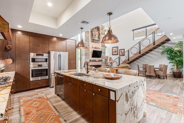 kitchen featuring a kitchen island with sink, sink, light hardwood / wood-style flooring, appliances with stainless steel finishes, and decorative light fixtures